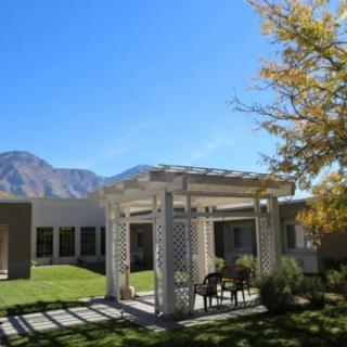A tranquil outdoor seating area under a pergola with a view of mountains and a building in the background.