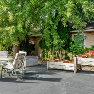 A cozy outdoor patio area surrounded by lush greenery and garden planters, featuring a table and chairs for relaxation.