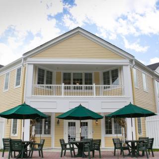 A two-story yellow house with a patio and outdoor seating under green umbrellas.