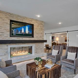 A modern living room with a stone wall and a fireplace under a mounted TV, featuring comfortable armchairs and a stylish coffee table.