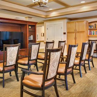 A conference room setup with neatly arranged chairs facing a television, surrounded by wooden furniture and a bookshelf.