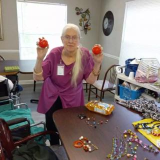 An elderly woman holding two red decorations while engaging in a craft activity indoors.