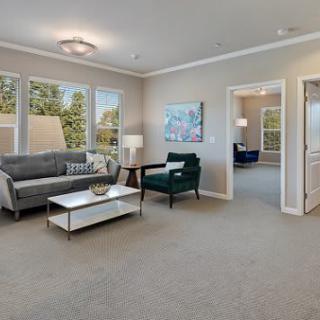 A modern living room with a grey sofa, green armchair, and a sleek coffee table, featuring large windows and neutral decor.