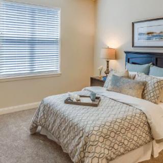A cozy bedroom with a neatly made bed, soft lighting from a bedside lamp, and framed artwork above the headboard.