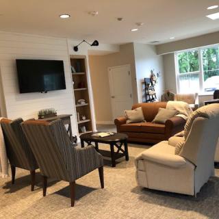 A cozy living room with sofas, armchairs, a TV, and large windows providing natural light.