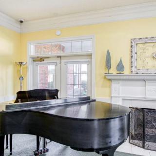 A cozy living room features a grand piano and a fireplace with decorative artwork, set against soothing yellow walls.
