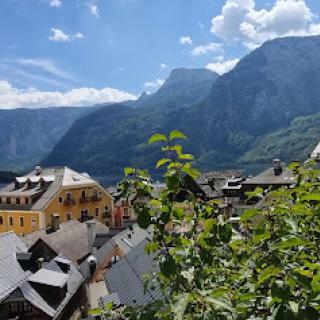 A picturesque view of a village nestled between majestic mountains, showcasing lush greenery and a bright blue sky.