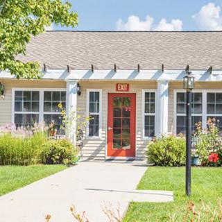 A charming house with a red door, surrounded by a well-maintained garden under a clear blue sky.
