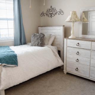 A cozy bedroom with a single bed, white dresser, and decorative elements.