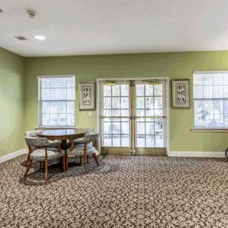 A cozy room with green walls, a round table with chairs, and large windows providing natural light.