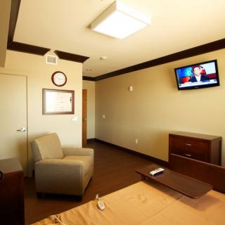 A hospital room with a bed, chair, and wall-mounted television.
