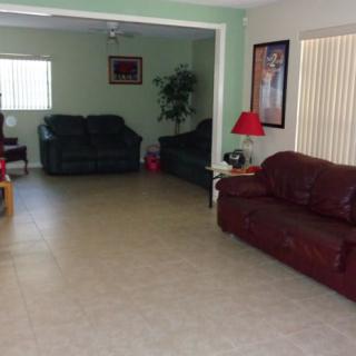 A spacious living room with sofas, a red lamp, and large windows with blinds.