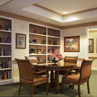 A cozy library corner with a round table surrounded by chairs and filled with bookshelves.