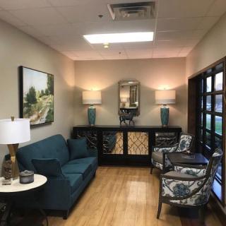 A cozy waiting area featuring a sofa, chairs, lamps, and artwork on the wall.