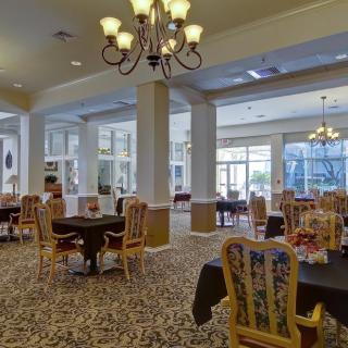 A spacious dining area with elegant chandeliers, tables, and chairs set on a carpeted floor.