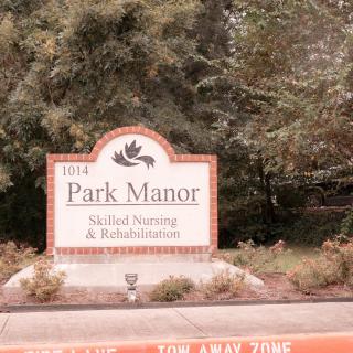 A sign for Park Manor Skilled Nursing & Rehabilitation surrounded by trees.