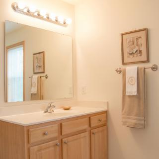 A clean and simple bathroom with a large mirror, wooden cabinets, and a towel rack.