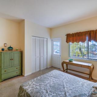 A cozy bedroom with a window allowing natural light, featuring a green dresser and a bed with a patterned bedspread.