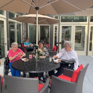 Seniors enjoying a pleasant day outdoors, sharing food and conversation under an umbrella.