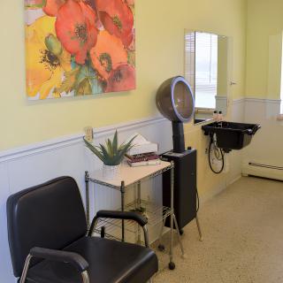 A cozy hair salon with a chair, hairdryer, and sink, decorated with vibrant artwork and a potted plant.