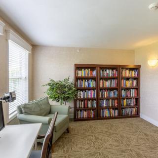 A cozy library corner with bookshelves, a comfortable chair, and a computer desk by the window.