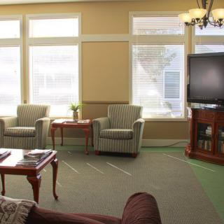 A cozy living room featuring chairs, a coffee table, and a television with large windows letting in natural light.