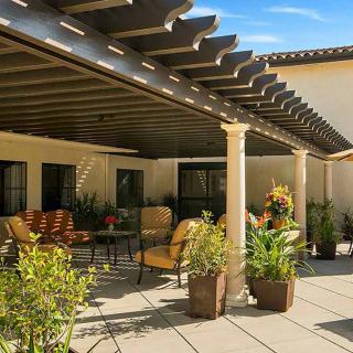 A cozy outdoor patio with a pergola providing shade, surrounded by plants and comfortable seating.
