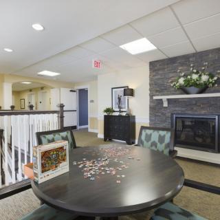 A cozy living room with a fireplace, round table, and chairs, featuring a partially completed puzzle on the table.