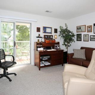 A cozy home office with a desk, chair, and sofa in a well-lit room.