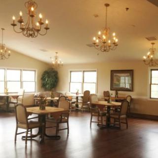 An elegant dining room with chandeliers, wooden floors, and multiple tables and chairs.