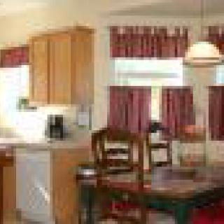 A cozy kitchen and dining area with wooden cabinets, a dining table, chairs, and red curtains.