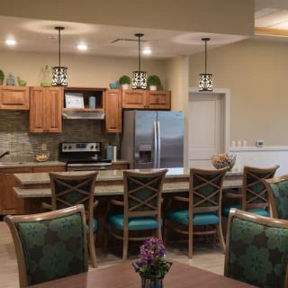 A modern kitchen and dining area featuring wood cabinets, stainless steel appliances, bar stools, and pendant lights.