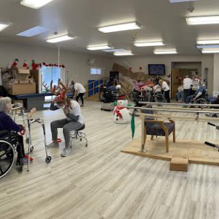 A spacious rehabilitation therapy room filled with elderly individuals engaging in various activities.