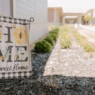 A decorative 'Home Sweet Home' sign placed in a garden by a pathway.