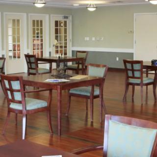 A spacious dining area with several wooden tables and chairs arranged neatly, set on a polished hardwood floor.