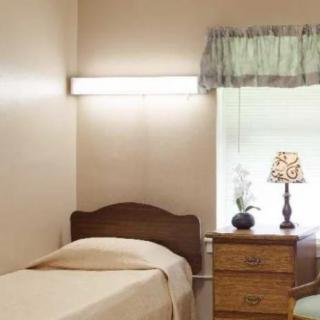 A simple bedroom with a single bed and a nightstand beneath a window.