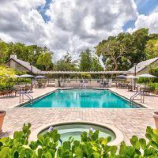 A serene outdoor swimming pool area surrounded by lush greenery and under a partly cloudy sky.