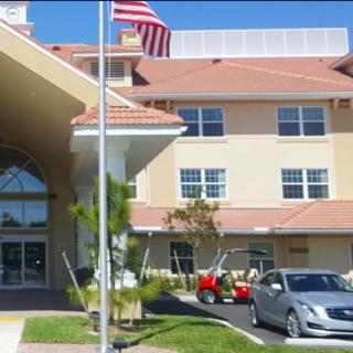 A hospital building with a car parked in front and an American flag waving above.