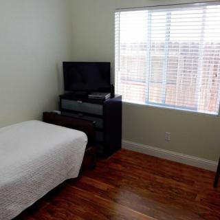 A minimalist bedroom with a single bed, dresser, and television next to a window.