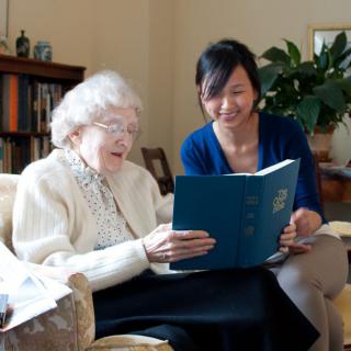 An elderly woman reading a book with the assistance of a younger woman.