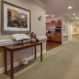 A cozy hallway with a wooden table displaying an open book and decorative items, leading to a kitchen area.