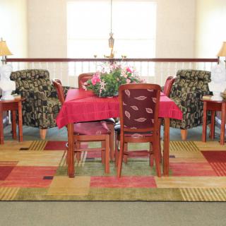 A cozy dining area with a table and chairs, adorned with a red tablecloth, surrounded by patterned armchairs and set on a colorful carpet.
