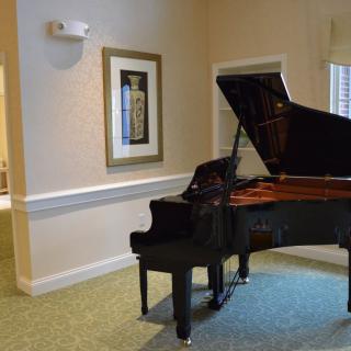 A grand piano in a well-lit interior room with artwork on the wall.