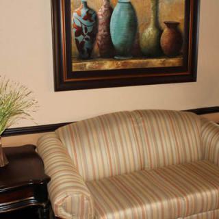 A cozy interior with a striped sofa, a framed painting of vases, and a table adorned with decorative plants.