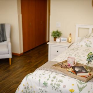 A cozy bedroom setup with a breakfast tray on the bed, featuring a comfortable armchair and wooden flooring.