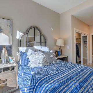 A cozy bedroom with blue bedding, decorative pillows, and a stylish mirror above the bed.