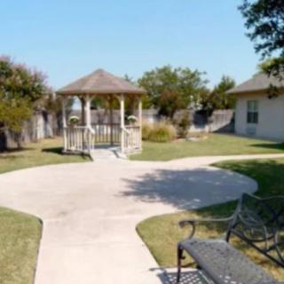 A sunny garden with a gazebo and benches along a paved pathway.