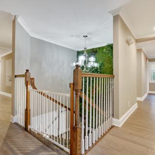 A modern interior hallway featuring a wooden staircase with white railings and a chandelier.
