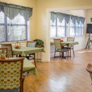 A cozy dining area with tables and chairs, featuring large windows and decorative curtains.