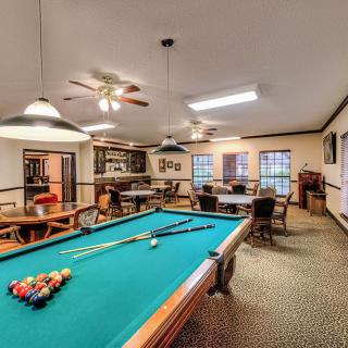 A cozy recreational room featuring a pool table and comfortable seating, illuminated by ceiling lights and fans.